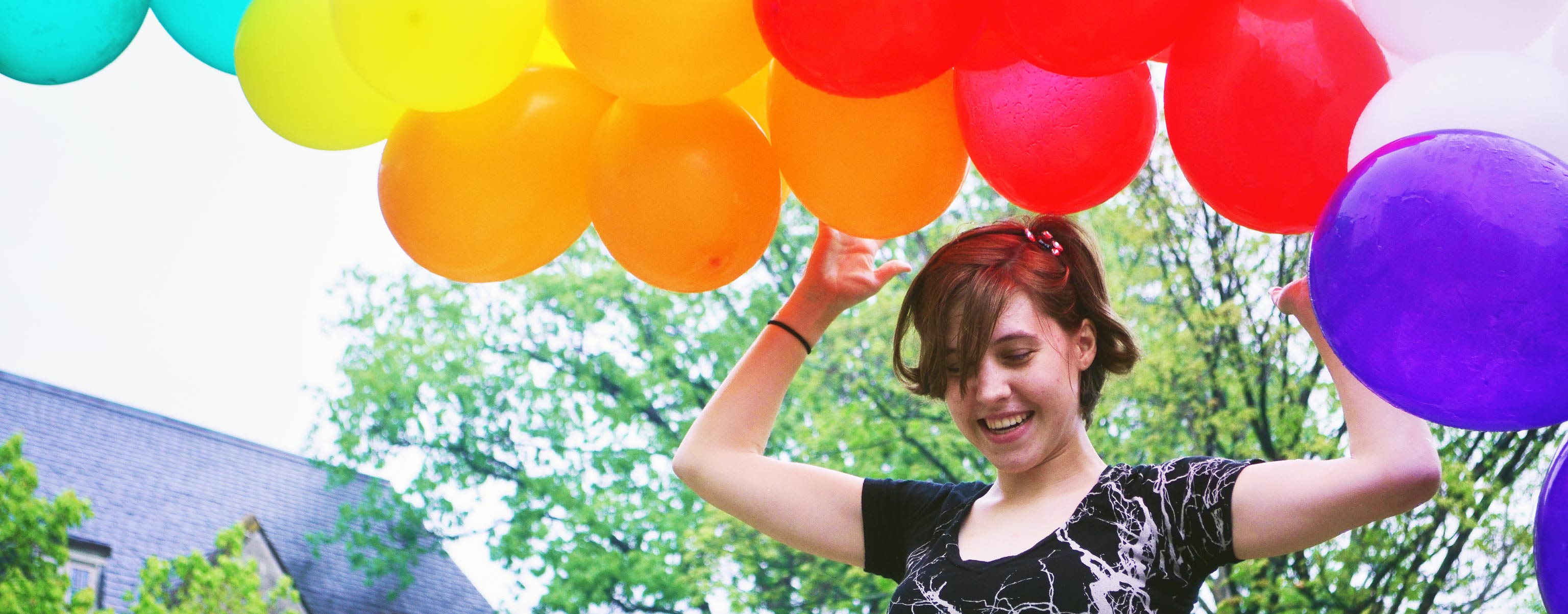 Brunette female student smiles while holding a large bunch of colorful balloons