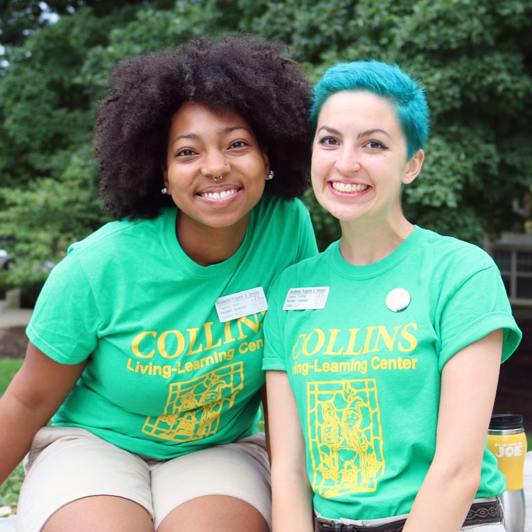 Two female students in Collins Center t-shirts smile and pose for the camera