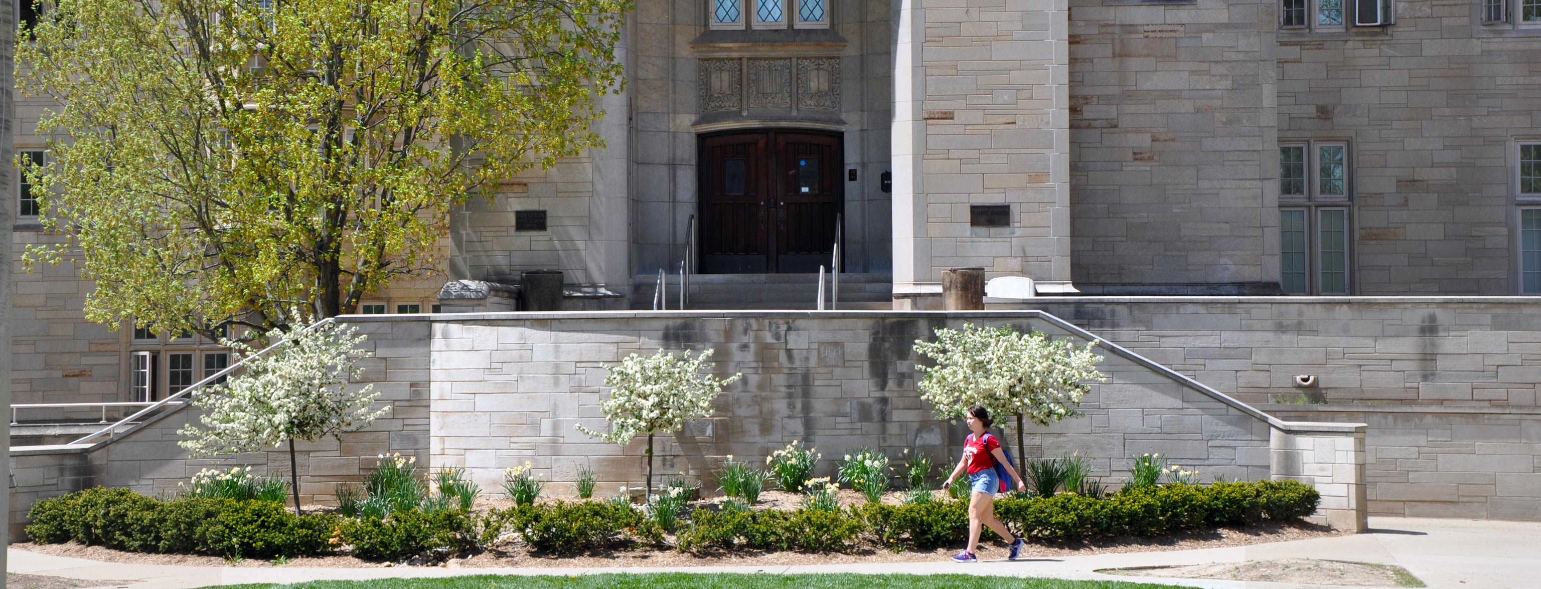 A student walking by the steps to the main entrance of the Collins Center