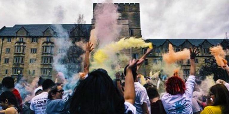 Students in front of the Collins Center throw colored powdered into the air